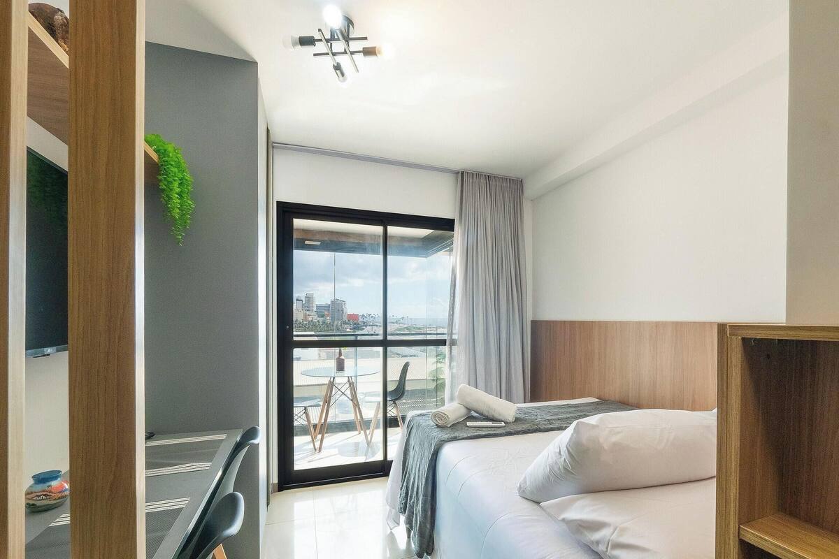 A modern hotel room with a bed, a desk, and a view of the cityscape.