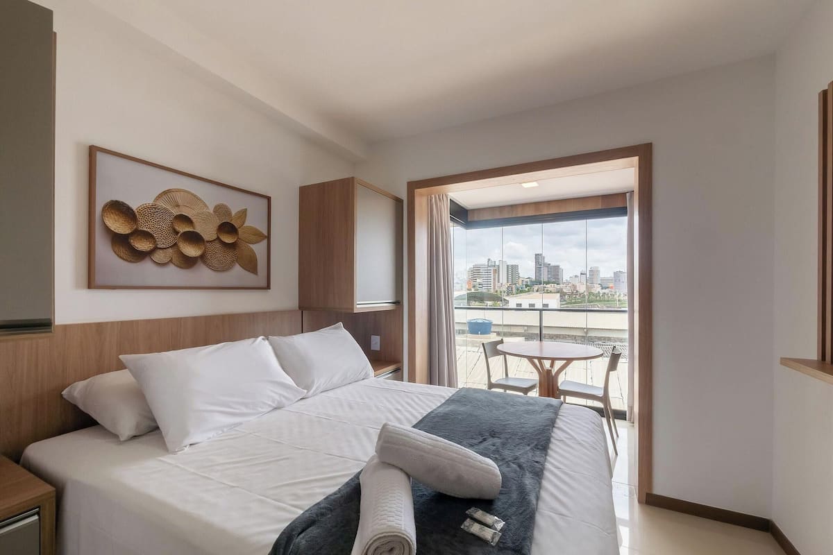 A hotel room with a bed, a view of the city, a balcony with a table and chairs, and a decorative wall piece.