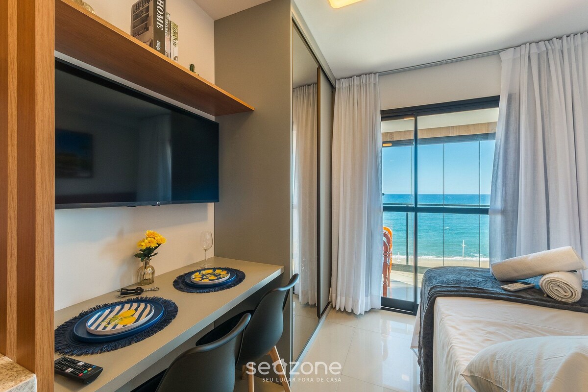 A hotel room with a balcony, a bed, a desk with a chair, and a TV.