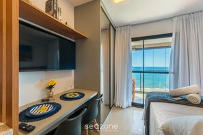 A hotel room with a balcony, a bed, a desk with a chair, and a TV. - Studios in Building w/ Pool and Gym - Jdns (Salvador)