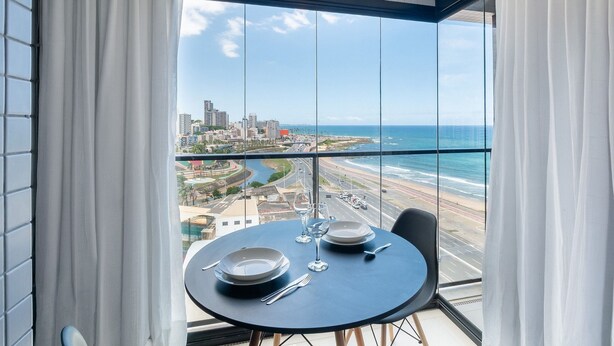 Un balcon avec une table dressée pour deux personnes, offrant une vue sur le paysage urbain de la côte.
