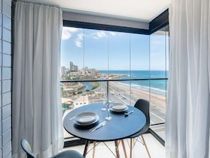 A balcony with a table set for two, overlooking a coastal cityscape. - Studios in Building w/ Pool and Gym - Jdns (Salvador)