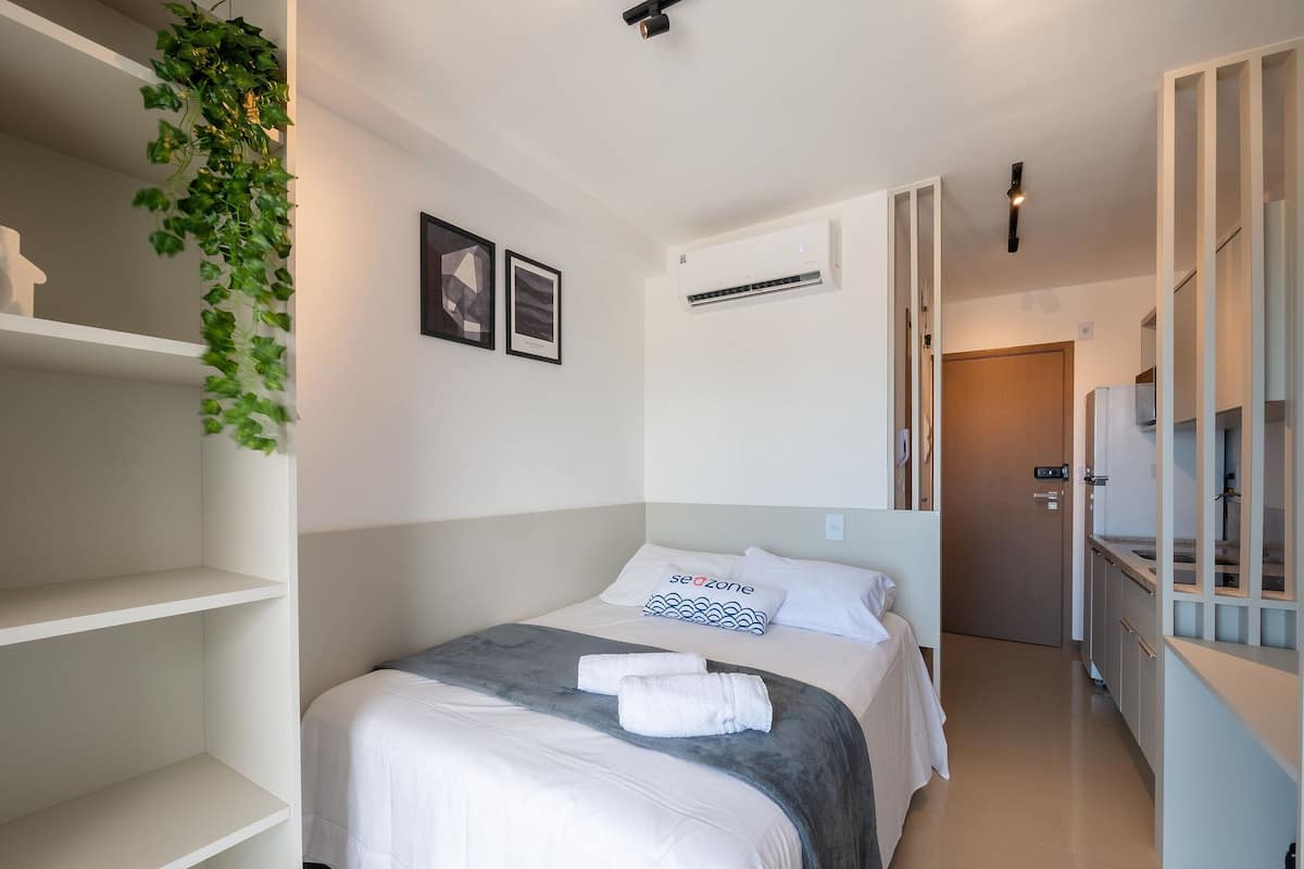 A modern hotel room with a bed, a wall-mounted air conditioner, and a hallway leading to a bathroom.
