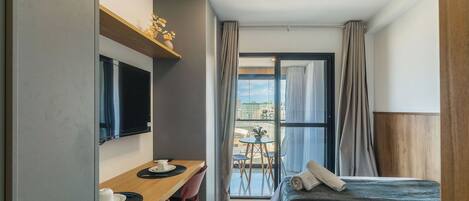 Une chambre d’hôtel comprenant un lit, un bureau avec des chaises, une télévision et un balcon avec une table et des chaises.
