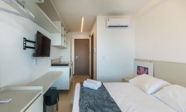 Een hotelkamer met een bed, een aan de muur bevestigde televisie, een kitchenette en een airconditioning.