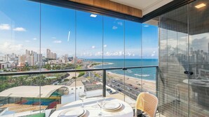 Un balcon avec une table dressée pour le dîner, offrant une vue sur un paysage urbain côtier avec des bâtiments et une plage.