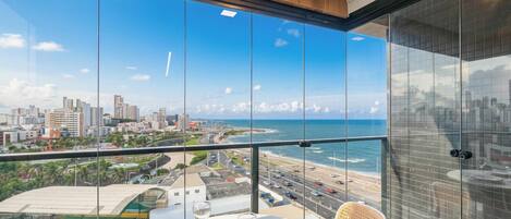 A balcony with a table set for dining, overlooking a coastal cityscape with buildings and a beach.