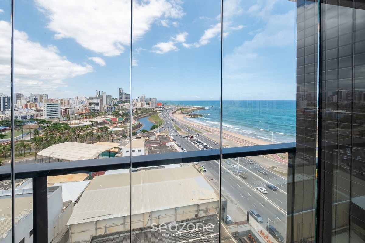 A high-rise building with a view of a coastal cityscape, including a beach and a river.