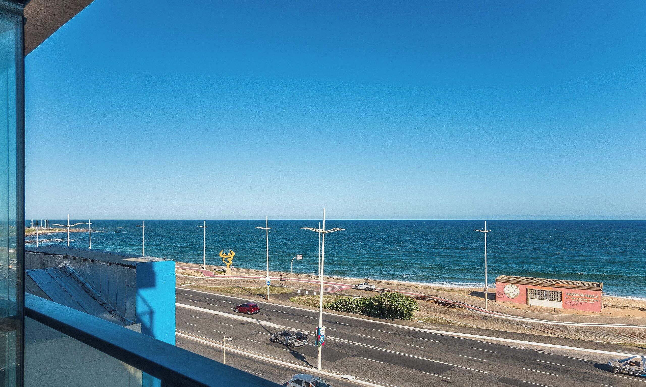 A coastal road with a view of the sea, a pedestrian path, and a small building with a clock.