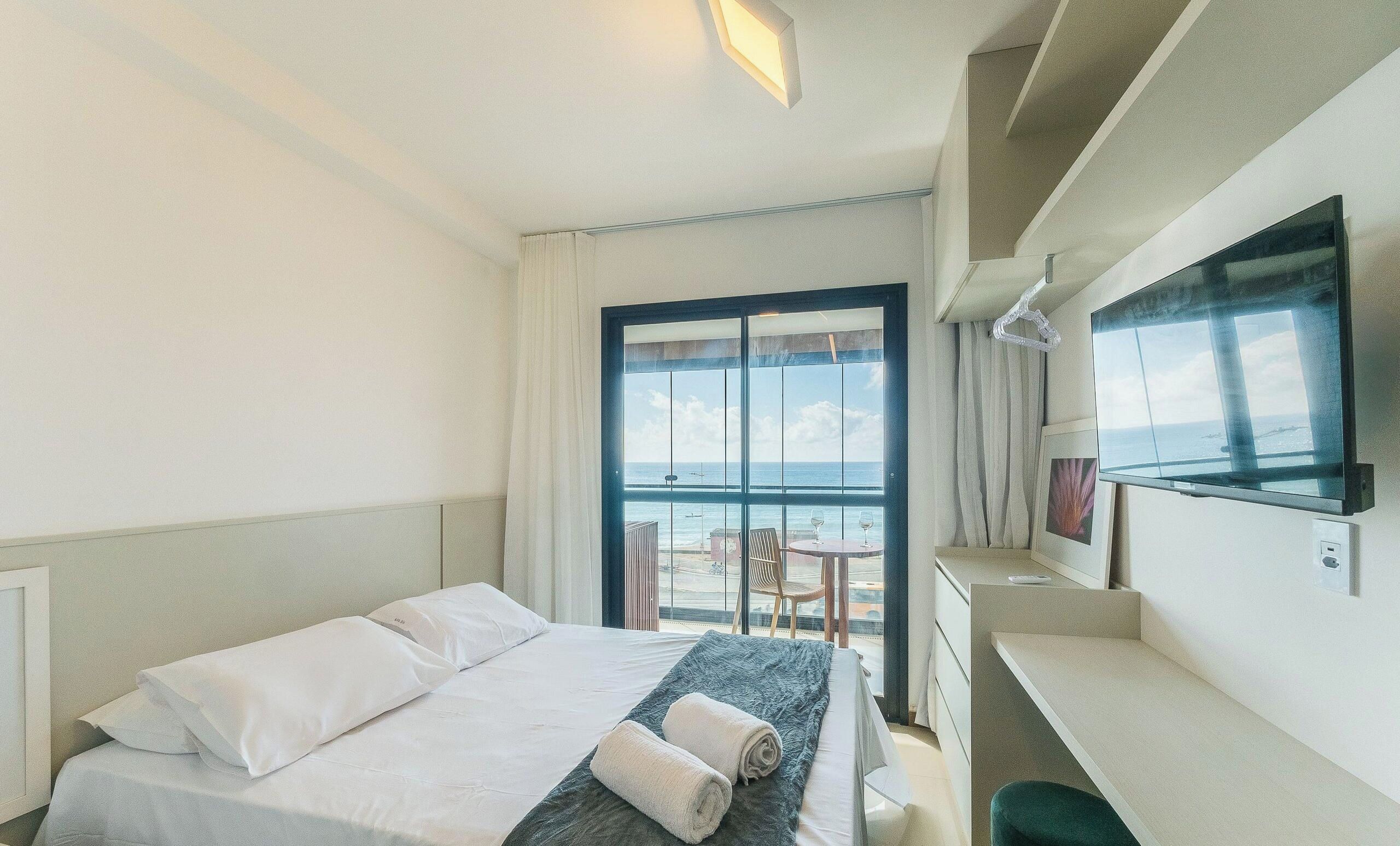 Habitació d'hotel amb un llit, escriptori, cadira i una finestra gran que ofereix vistes al mar.