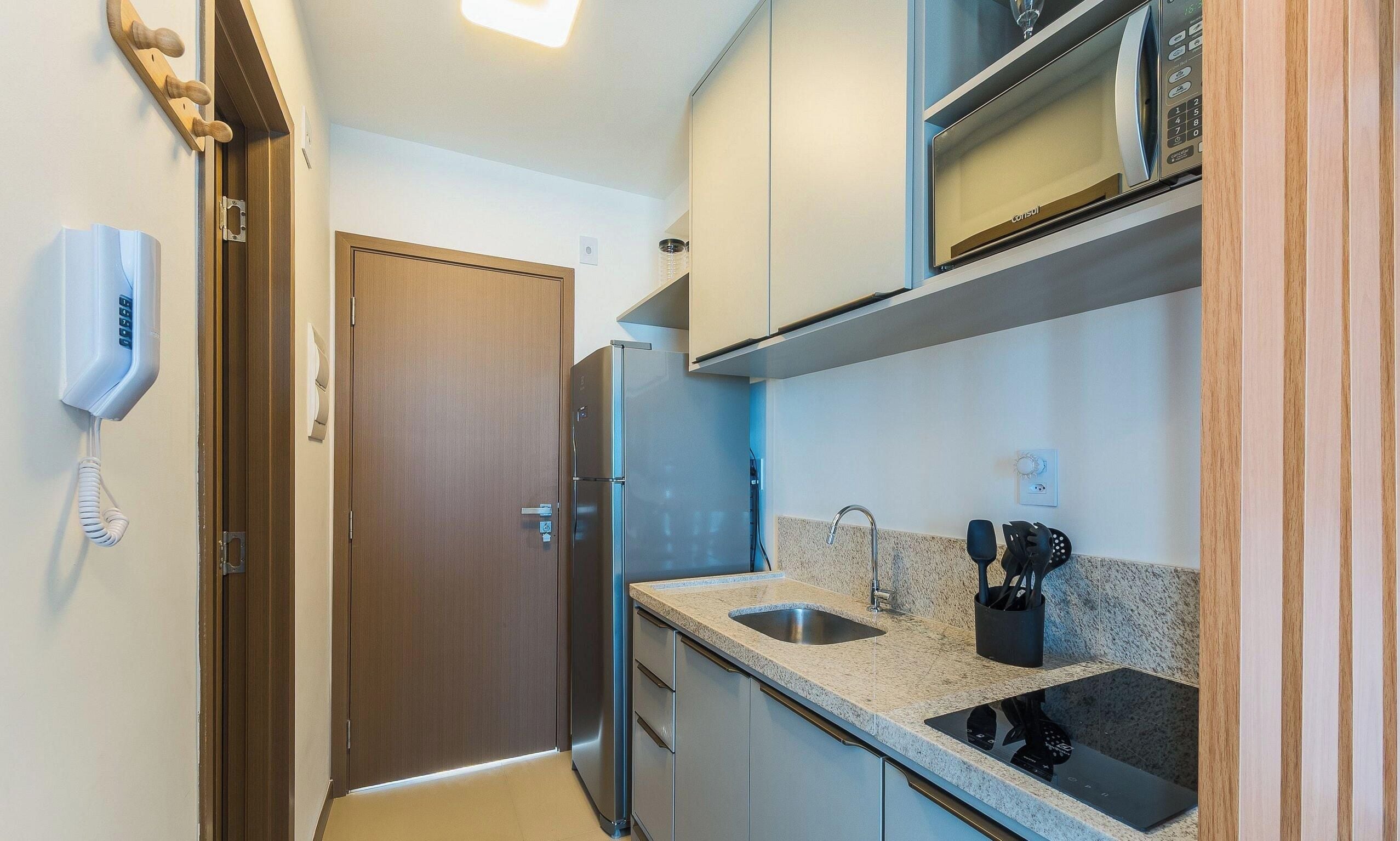A compact kitchen with a refrigerator, microwave, and a sink with a faucet.