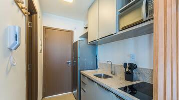 A compact kitchen with a refrigerator, microwave, and a sink with a faucet.