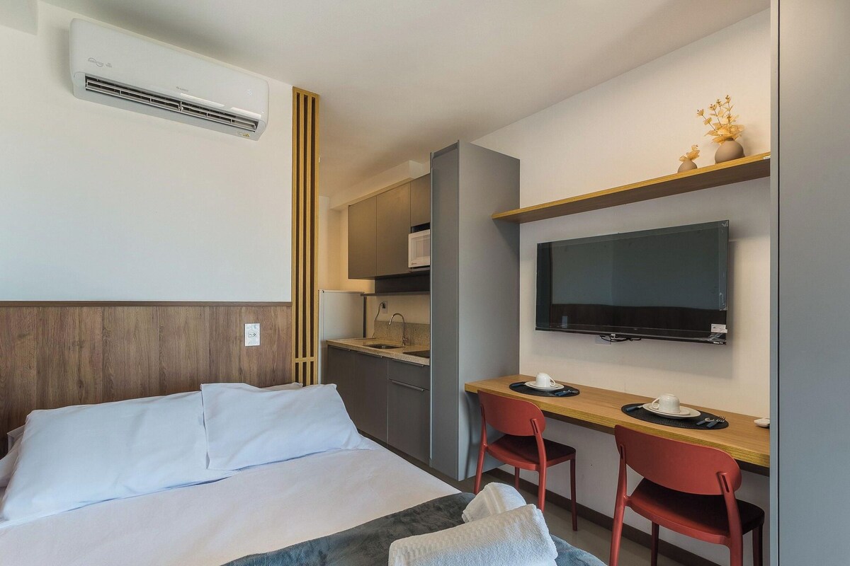 A hotel room with a bed, a desk, a chair, a television, and a kitchenette.