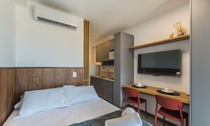 A hotel room with a bed, a desk, a chair, a television, and a kitchenette. - Studios in Building w/ Pool and Gym - Jdns (Salvador)