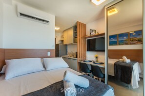 A hotel room with a bed, a desk, a chair, and a small kitchenette. - Studios in Building w/ Pool and Gym - Jdns (Salvador)