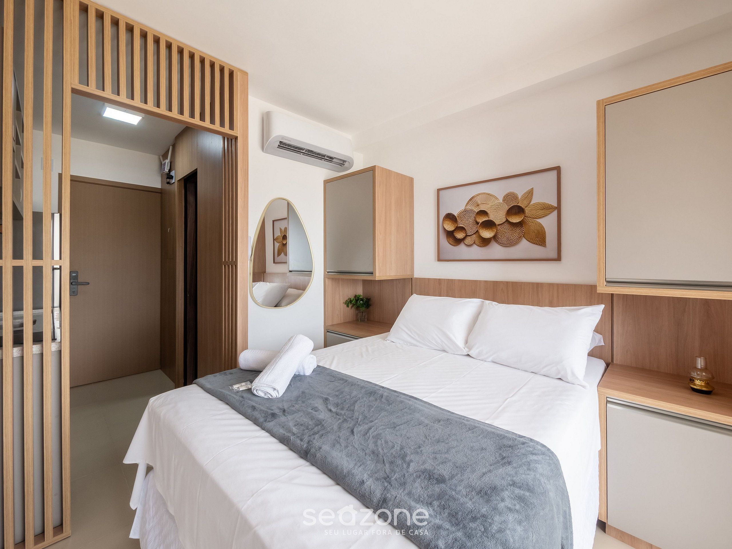 Une chambre d’hôtel équipée d’un lit, d’un miroir, d’un climatiseur, d’une table de chevet et d’une œuvre d’art accrochée au mur.