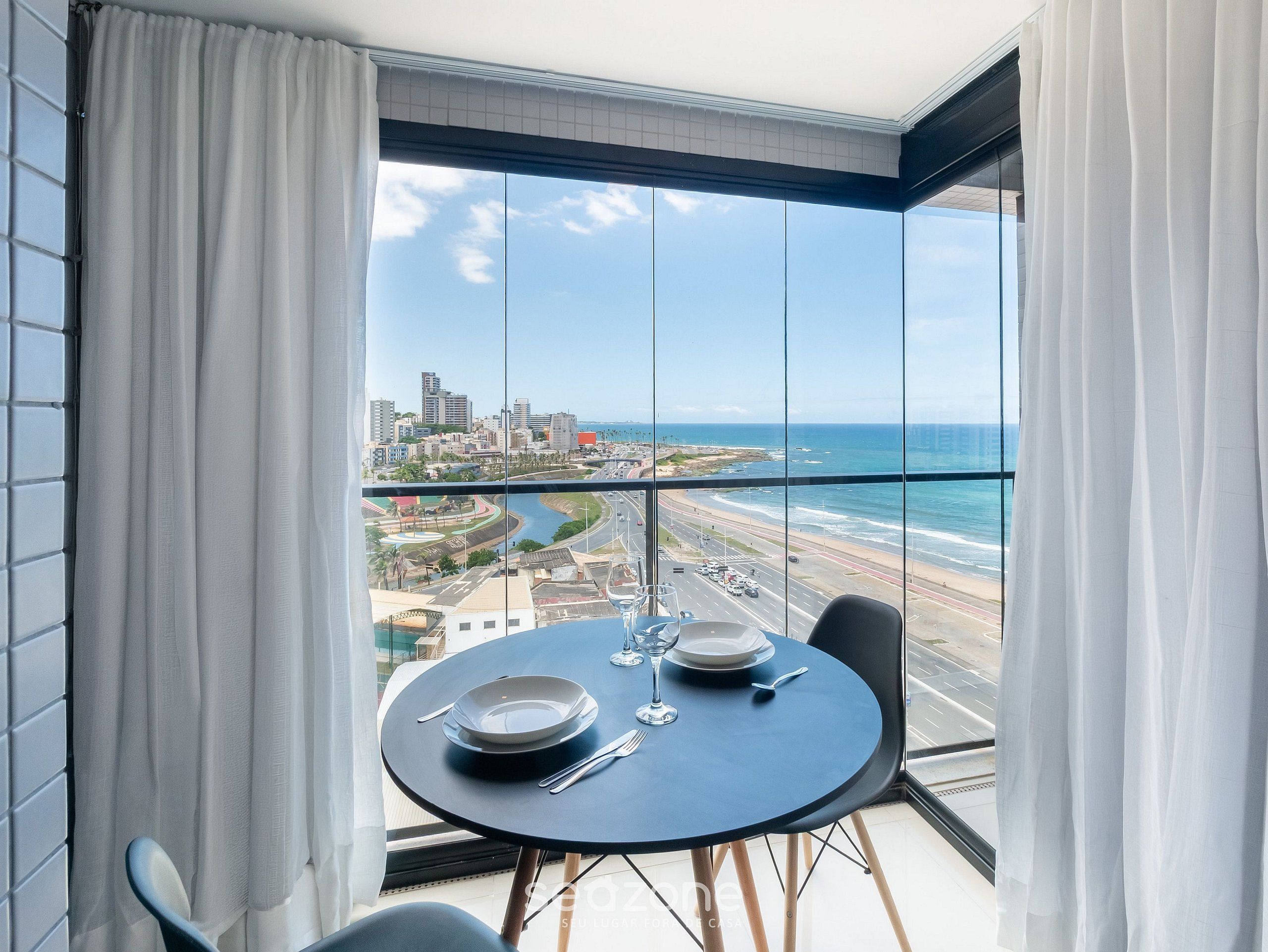 A balcony with a table set for two, overlooking a coastal cityscape.