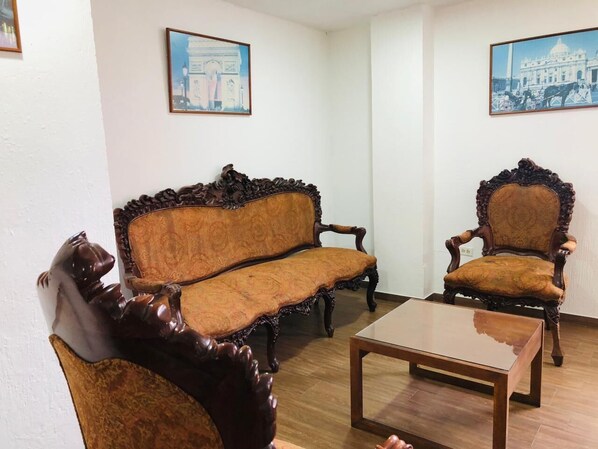 A room with a wooden sofa, a matching armchair, and a small table. There are two framed pictures on the walls. - Urban Colonial (Quito)