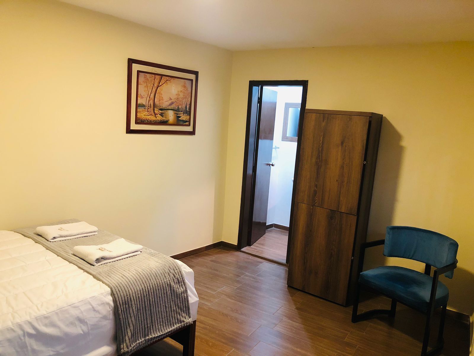Een hotelkamer met een bed, een stoel, een kledingkast en een schilderij aan de muur.