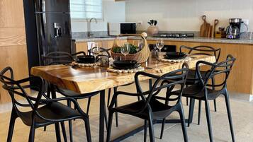 A modern kitchen with a wooden dining table, black chairs, a black refrigerator, and a hanging light fixture.