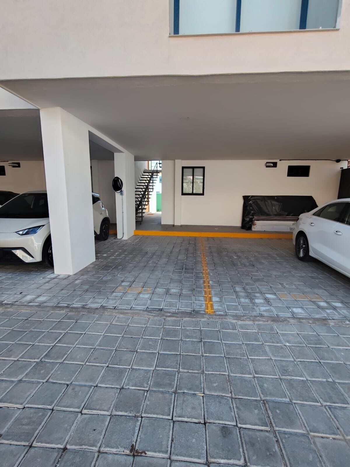 Ett parkeringsgarage med två vita bilar parkerade, en trappa som leder upp till en övre våning och en gul linje på golvet.