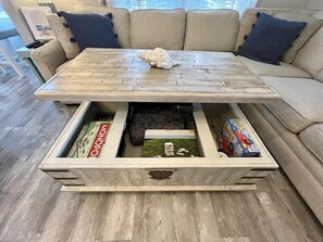 A wooden coffee table with storage drawers containing board games and a decorative shell. - P35 The Sand Bucket Retreat (Myrtle Beach)