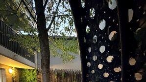 Une cour avec un espace aménagé pour s’asseoir, un arbre et une clôture décorative.
