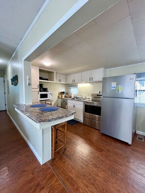 A kitchen with white cabinets, a stainless steel refrigerator, a built-in oven, and a granite countertop. - 1625 Coastal Cottage (Myrtle Beach)
