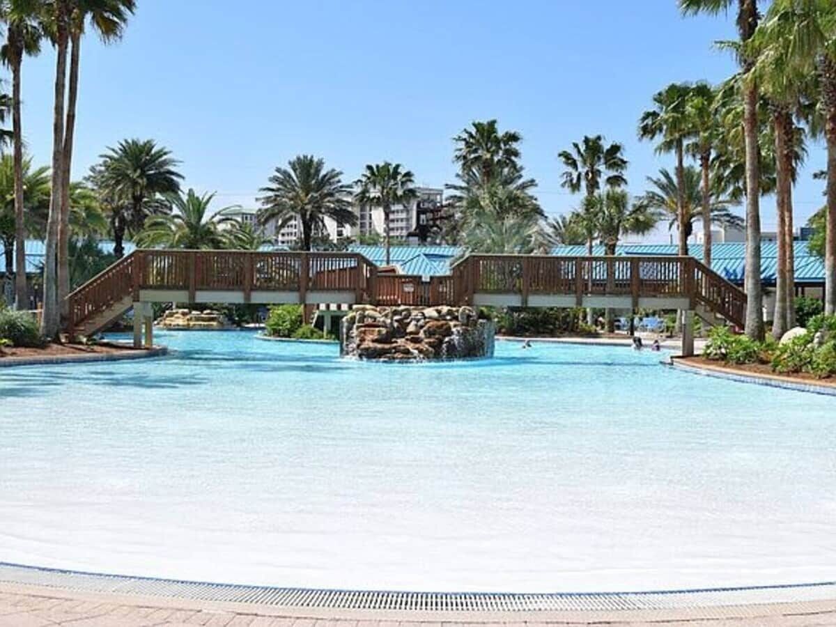 A large pool with a wooden bridge and palm trees.