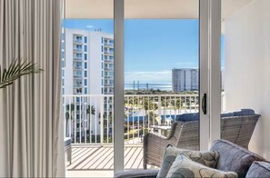 A balcony with wicker furniture, a sliding glass door, and a view of high-rise buildings and a beach. - Two King BR, Beautiful Resort Pool, Gulf View (Destin)