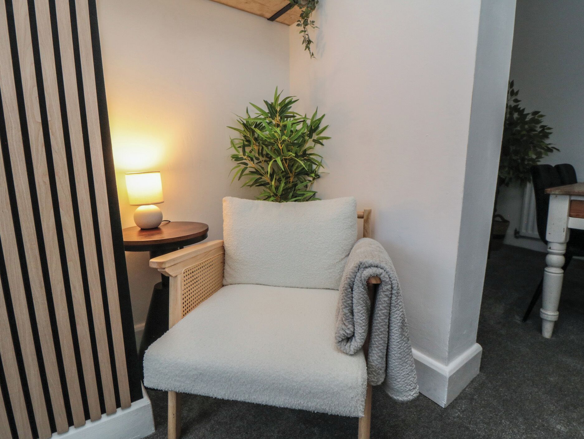 Une pièce confortable avec un fauteuil, une petite table sur laquelle se trouve une lampe, et une plante en pot.