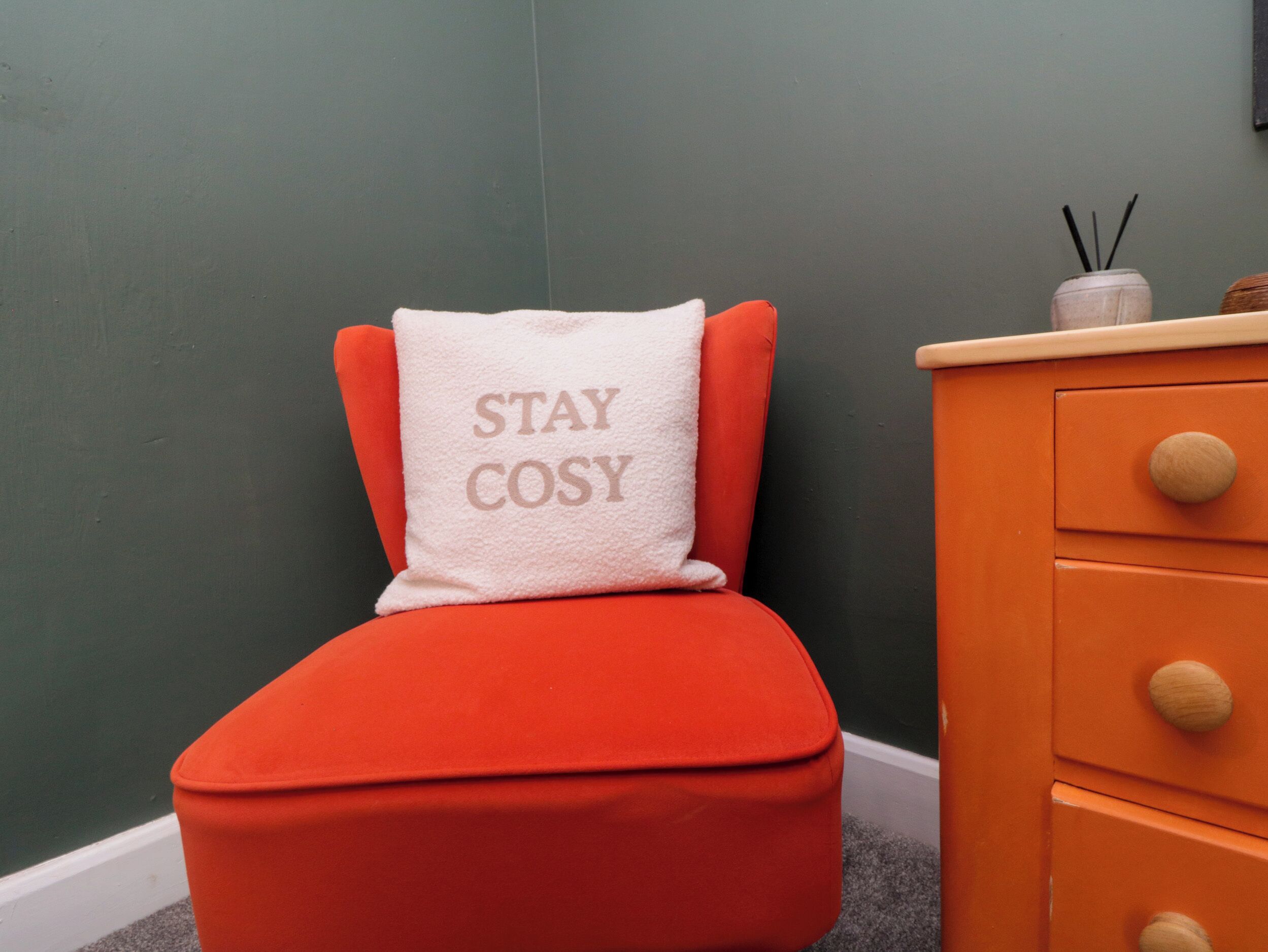A small orange chair with a white cushion that has the text 'STAY COSY' on it.