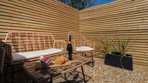 A wicker lounge chair with a cushion, a bottle of wine, and a glass on a glass table. - Islas Sea Forge (Saltburn-by-the-Sea)
