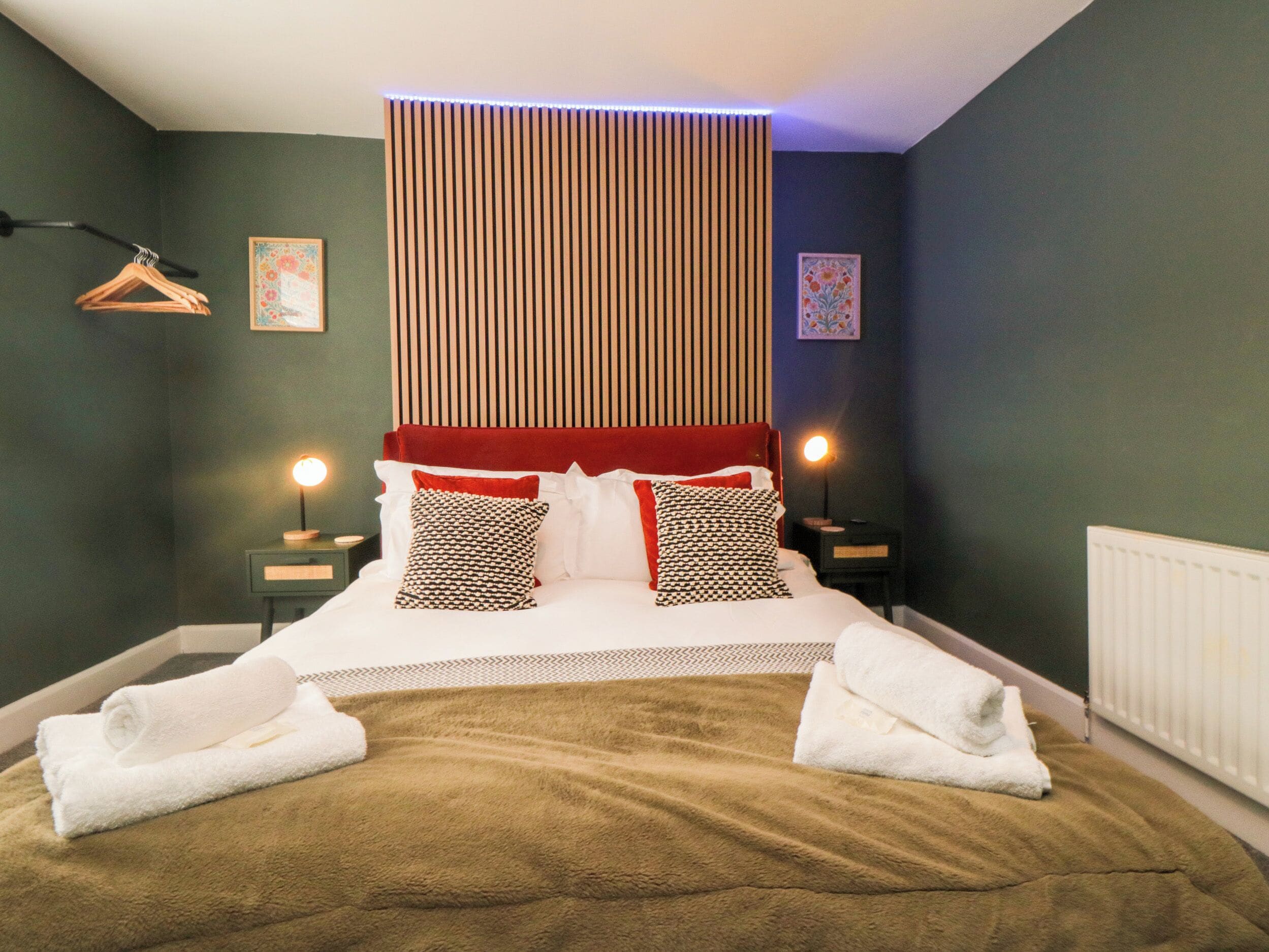 A bedroom with a bed, two bedside tables, a hanging light fixture, and a radiator.