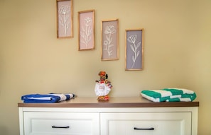 A room with a wooden dresser, a small figurine, and three framed floral artworks on the wall. - O.L.S Property: Modern 2-bedroom home in Paynter’s with AC and Free Parking! (Piggotts/ Paynter’s Estate)