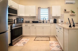 A modern kitchen with white cabinets, stainless steel appliances, and a window with curtains. - O.L.S Property: Modern 2-bedroom home in Paynter’s with AC and Free Parking! (Piggotts/ Paynter’s Estate)