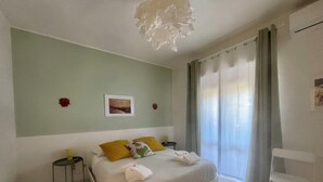 A bedroom with a bed, a bedside table, a chair, a picture on the wall, and a window with curtains.