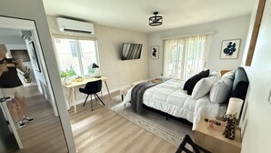 A modern bedroom with a bed, desk, and chair, a large window, and a view of the outdoors.