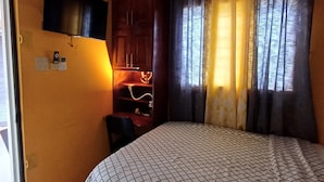 A bedroom with a bed, a TV mounted on the wall, an air conditioning unit, a desk with a chair, and a window with curtains. - Harbour View Inn, A Piece Of
Paradise (Harbour View)