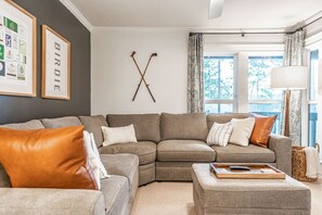 A living room with a sectional sofa, a coffee table, and a wall-mounted hockey stick display.