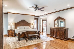 Ein geräumiges Schlafzimmer mit einem großen Bett, einem Holz-Kopfteil, einer Bank, einem Schminktisch und einem Deckenventilator.