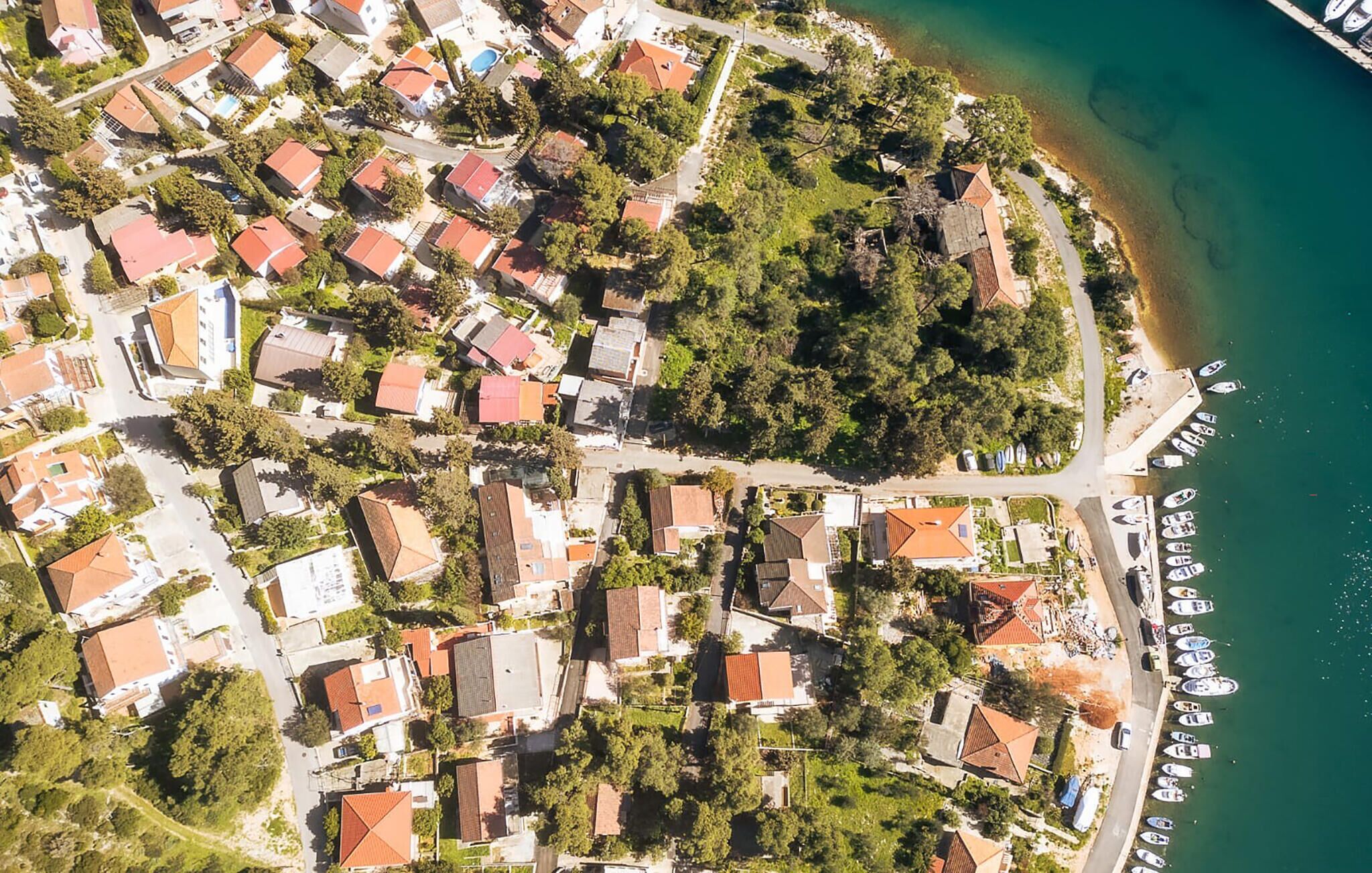 An aerial view of a coastal residential area with houses, a road, and boats docked along the shore.