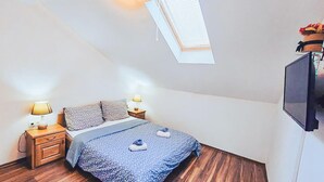 A bedroom with a sloped ceiling, a skylight, a bed with a blue floral bedspread, two bedside lamps, and a TV mounted on the wall. - Awesome apartment in Vrboska with WiFi (Vrboska)