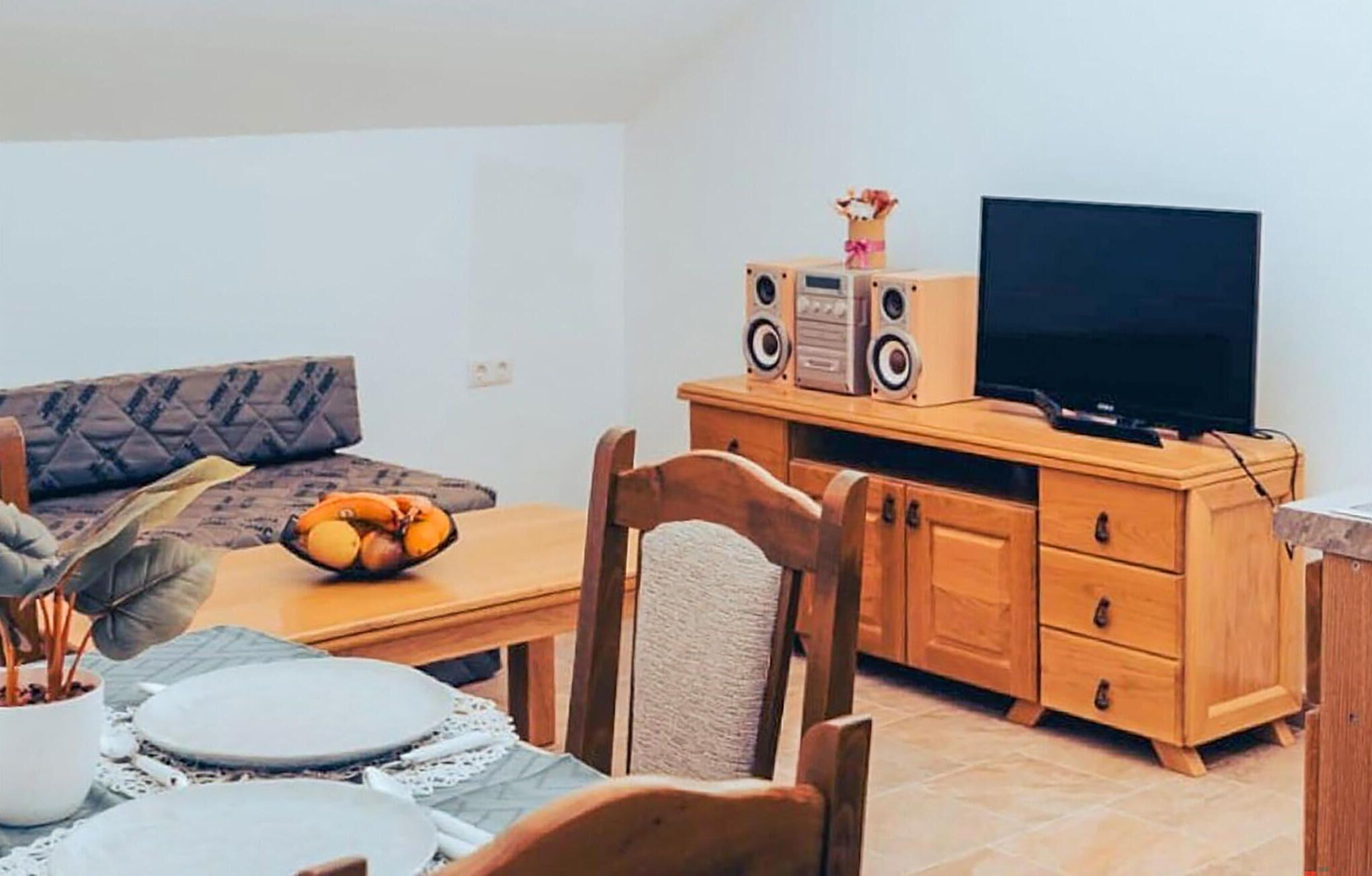 A living room with a sofa, wooden cabinet, TV, and a table with a bowl of fruit.