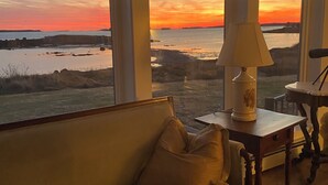 A living room with a sofa, a lamp, and a view of a sunset over the water. - OCEANFRONT New Custom Built 3Bdrm Handicap Accessible Home VIEWS & BEACH ACCESS (Jonesport)