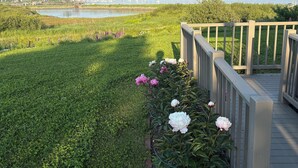 A landscaped garden with a wooden deck overlooking a body of water and distant land. - OCEANFRONT New Custom Built 3Bdrm Handicap Accessible Home VIEWS & BEACH ACCESS (Jonesport)