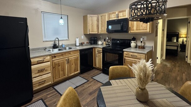 A modern kitchen with wooden cabinets, a black refrigerator, a microwave, and a dining area with a table and chairs.