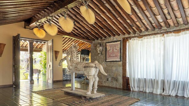 Ein Zimmer mit Fliesenboden, einer Statue, einer Decke mit Bambusdetails und einem zur Außenseite führenden Durchgang.