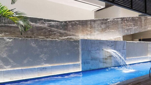 Ein Pool mit Wasserfall, umgeben von einer Betonmauer und einem gefliesten Boden.