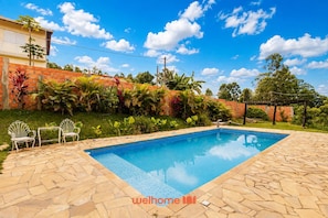 A rectangular swimming pool with a tiled edge, surrounded by a stone patio. There are two white metal chairs and a small table on the patio. - Chácara em Mairinque com Churrasqueira e Piscina (Alumínio)